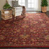 Living room scene with a brick red Nourison Jewel Brick Persian rug, cream chair, and dark wood floors.