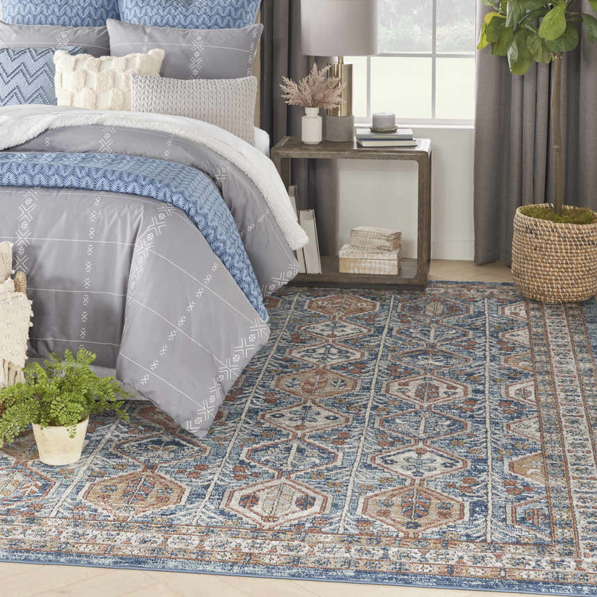 Bedroom scene with Nourison Quarry Blue Multicolor rug, gray bedding, wood side table, and natural light.