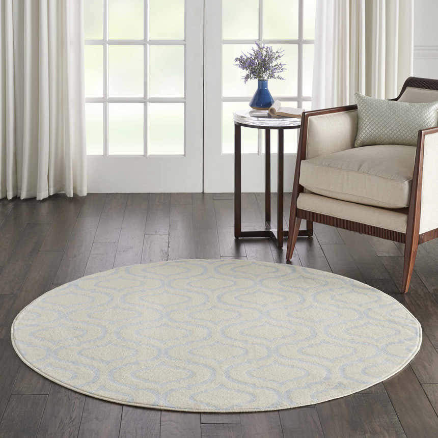 Living room scene with a round Nourison Jubilant Ivory Blue rug, chair, side table, and dark wood floors.