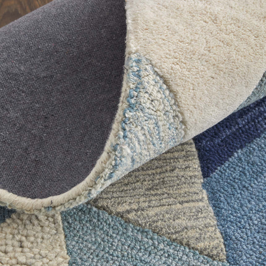 Close-up of the Feizy Arazad rug showing its geometric blue, ivory, and gray pattern and hand-tufted texture. Fold