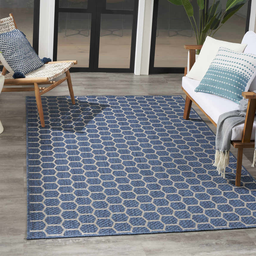 Modern patio scene with a Nourison Twist Blue Area Rug, wood furniture, and blue accent pillows.