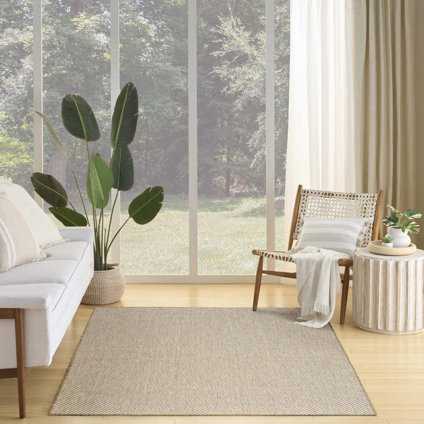 Living room scene with Nourison Courtyard Jute Ivory rug, white sofa, wood chair, and large window overlooking trees.