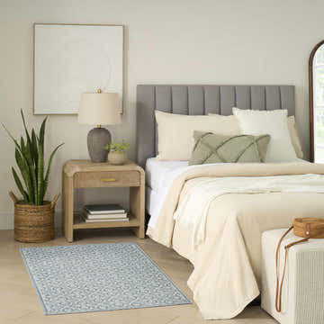 Bedroom scene with Nourison Charm Blue Ivory rug, neutral bedding, wood nightstand, and woven accents.