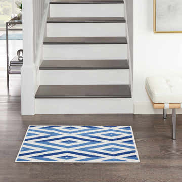 Entryway scene with Nourison Whimsicle Ivory Blue rug, wood floors, white stairs, and a modern white bench.