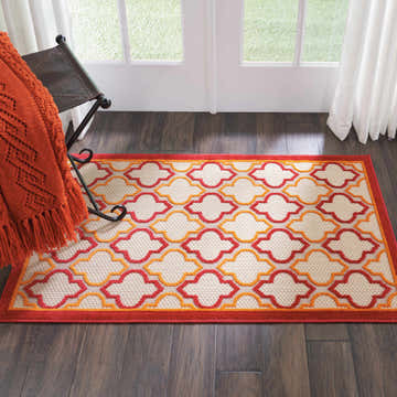 Entryway with Nourison Aloha Red Outdoor Area Rug, red and orange quatrefoil pattern, dark wood floor.