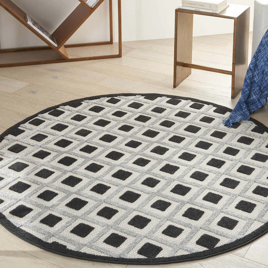 Modern living room scene with a round Nourison Aloha Black White Area Rug featuring a geometric square pattern.