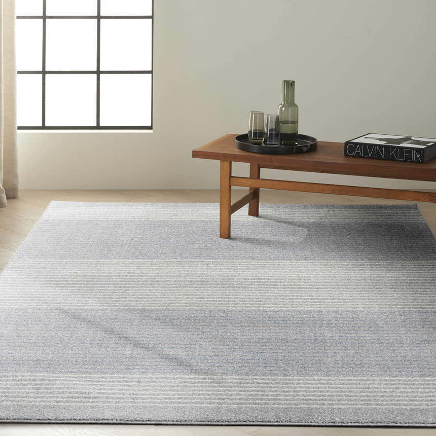 Minimalist room with Calvin Klein River Flow Grey rug, wood bench, and natural light. Modern style.