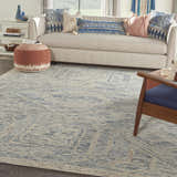 Living room scene with a Nourison Interlock Blue Multicolor rug, neutral sofa, blue pillows, and wood accents.