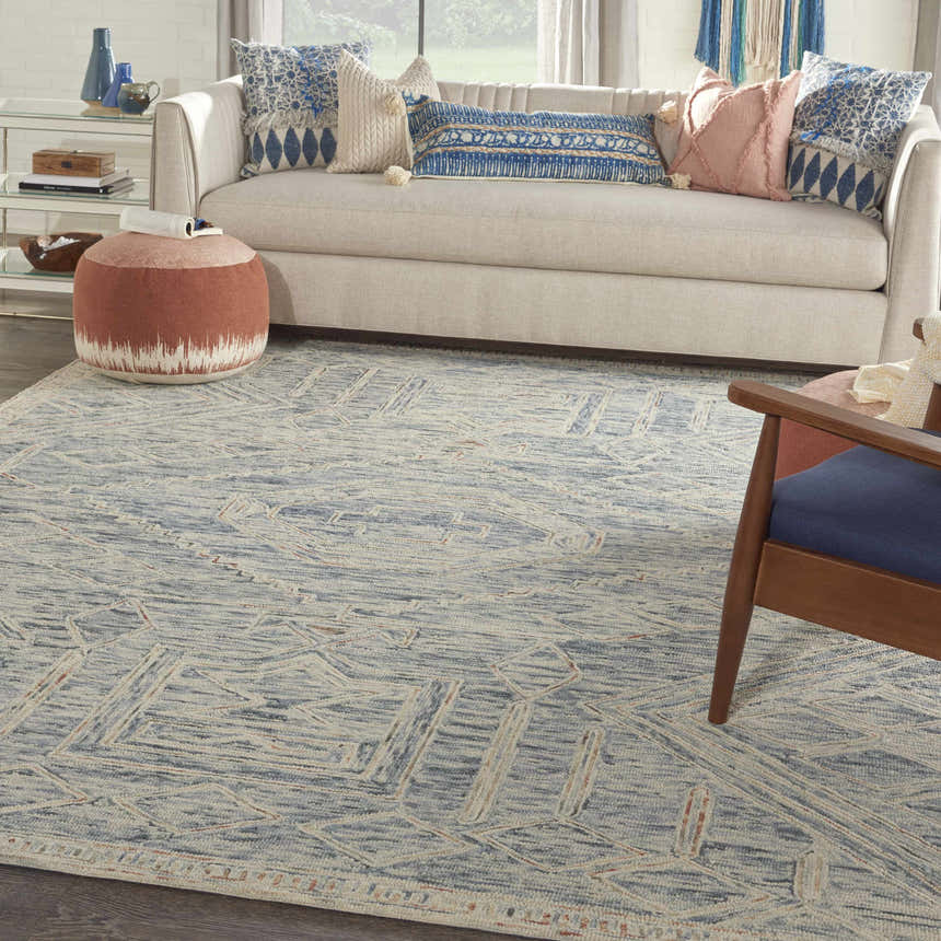 Living room scene with a Nourison Interlock Blue Multicolor rug, neutral sofa, blue pillows, and wood accents.