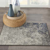 Styled room scene with Nourison Passion Charcoal Ivory rug, woven ottoman, and vases on wood floor.