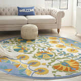 Living room scene with a round Nourison Aloha Multicolor rug, beige sofa, blue pillow, and knit pouf.