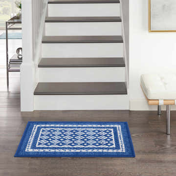 Entryway with Nourison Whimsicle Navy Farmhouse Indoor Area Rug, wood floors, white stairs, and a modern bench.