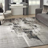 Living room scene with grey sofa and Nourison Twilight Grey Ivory Black rug, modern abstract design.
