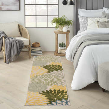 Bedroom scene with a Nourison Aloha Green Multicolor Tropical Area Rug runner, floral pattern, and neutral decor.