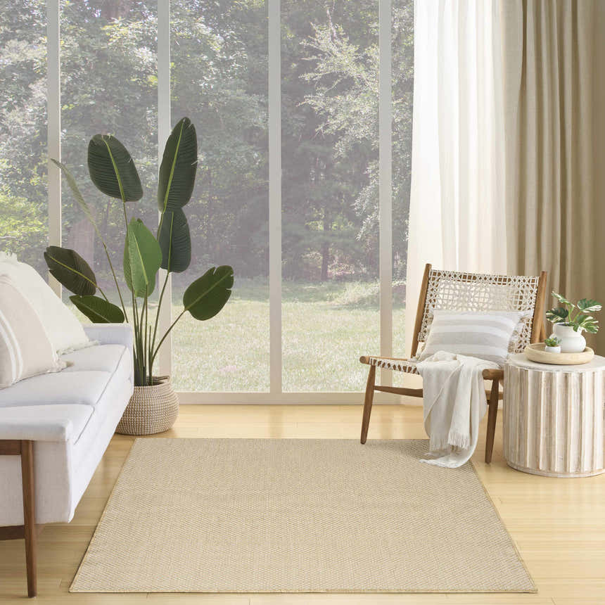 Living room scene with a Nourison Courtyard Jute Ivory rug, white sofa, wood chair, and a view of a lush green forest.