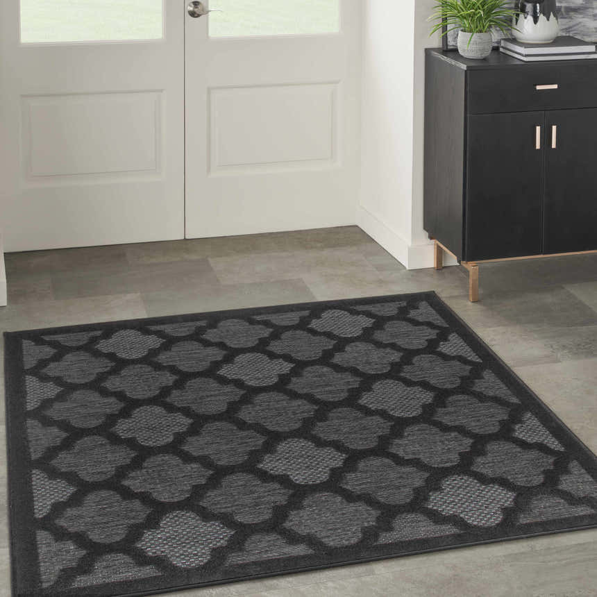 Entryway with a Nourison Easy Care Charcoal Black Modern Area Rug, black cabinet, and white door.