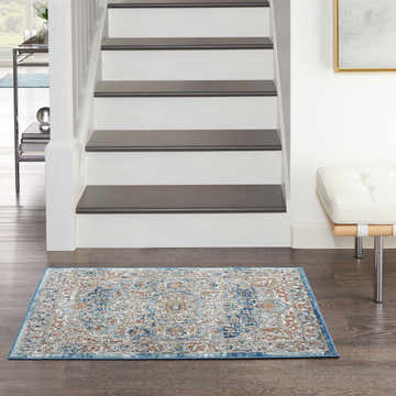 Entryway with Nourison Quarry Ivory Blue Vintage rug, dark wood floor, white stairs, and modern bench.