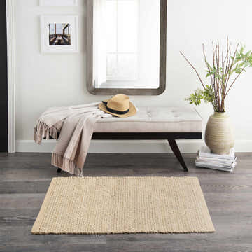 Entryway scene with a Nourison Natural Jute Bleached Farmhouse Indoor Area Rug, bench, mirror, and neutral decor.