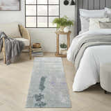 Bedroom scene with a Nourison Silk Shadows Blue Green rug, light wood floors, and neutral furniture. Modern, calming style.
