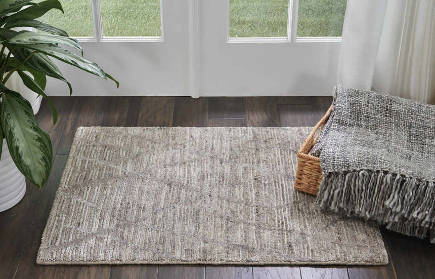 Entryway with ash Nourison OCEAN rug, dark wood floor, white door, plant, and throw blanket.