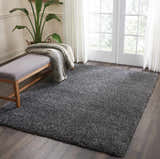 Bright room with Nourison Malibu Shag dark grey rug, wood floors, bench, and plant. Soft, cozy feel.