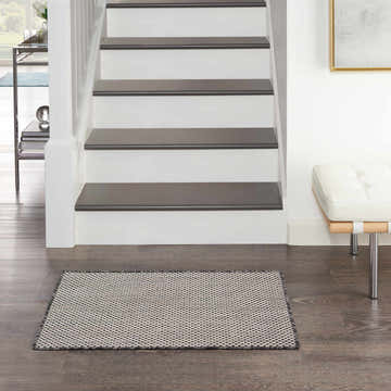 Entryway scene with a Nourison Courtyard Ivory Charcoal rug, dark wood floors, white stairs, and a white leather bench.