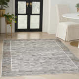 Entryway with Nourison Desire Charcoal Grey rug, wood floors, black door, gold planters, and round white table.