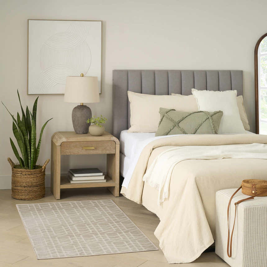 Bedroom scene with a Nourison Charm Silver Ivory Rug, wood nightstand, and neutral bedding.