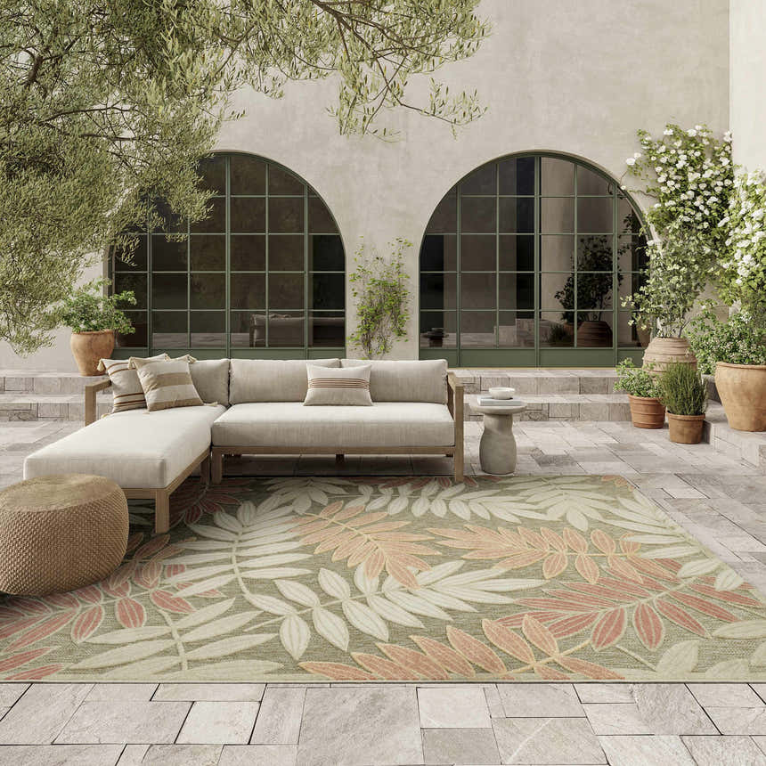 Outdoor patio with a beige sectional sofa and Nourison Aloha Sage Rose Rug featuring a leaf pattern.