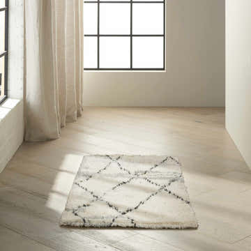 Minimalist room scene with a Calvin Klein San Antonio ivory Moroccan rug on light wood floors near window and curtains.