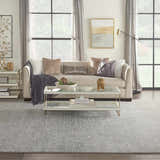 Living room scene with a grey Inspire Me! Home Decor Elegance area rug, sofa, glass coffee table, and natural light.