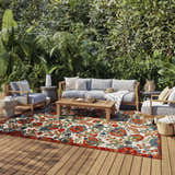 Outdoor patio scene with a Nourison Aloha Red Multicolor Farmhouse Area Rug, gray furniture, and lush greenery.
