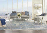 Light-filled living room with a Nourison Ellora Blue rug, gray sofa, glass table, and city view.
