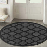 Entryway with a round Nourison Easy Care Charcoal Black rug, white door, and bench.