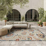 Outdoor patio scene with a Nourison Aloha Grey Multicolor Farmhouse Area Rug, sofa, and potted plants.