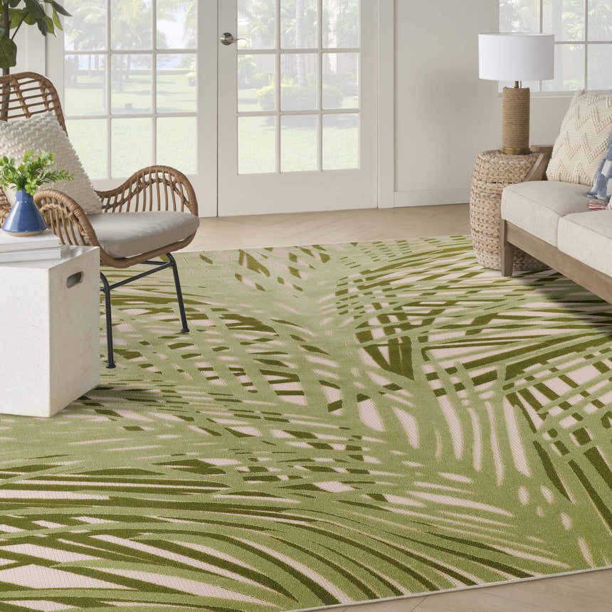 Coastal living room with a Nourison Aloha Ivory Green Outdoor Area Rug, wicker chair, and light wood sofa.