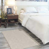 Bedroom scene with a Nourison Courtyard Ivory Silver rug, white bedding, and dark wood nightstand. Modern style.