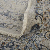 Close-up of the Feizy Kaia rug showing its damask pattern, blue, orange, and tan colors, and fringed edge. Fold