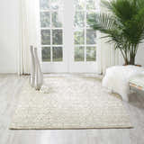 Sunlit room with Nourison Luminance Opal Vintage rug, silver vases, palm tree, and white bench. Serene, light-filled space.