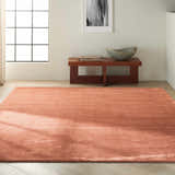 Minimalist room scene with a rust-colored Calvin Klein Home Lunar rug, wood bench, and neutral decor.