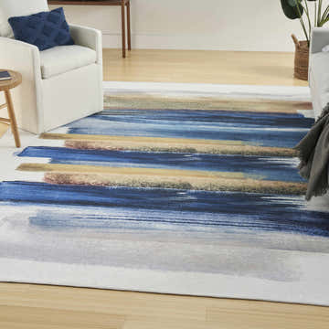 Living room scene with a Nourison Blue Multicolor Modern Indoor Washable Area Rug, white chairs, and light wood floors.