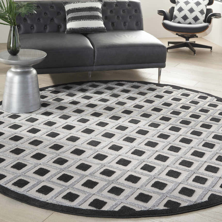 Modern living room with a round Nourison Aloha Black White area rug, black sofa, and stylish decor.