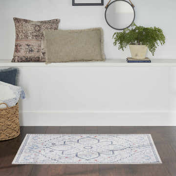 Farmhouse style room with Nourison New Concept Ivory Blue rug on dark wood floor. Pillows, plant, and mirror on white shelf.