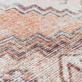 Close-up of the Arncliffe Washable Area Rug, showcasing its woven texture and bohemian zigzag pattern in orange, brown, and ivory. Texture