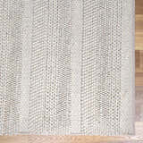Close-up of the cream Alora Area Rug showing its hand-woven texture and wool blend on a wood floor. Swatch