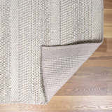 Close-up of cream Alora Area Rug showing hand woven texture and backing on wood floor. Contemporary style. Fold