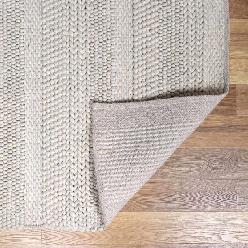 Close-up of cream Alora Area Rug showing hand woven texture and backing on wood floor. Contemporary style. Fold