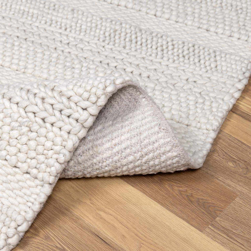 Close-up of the cream Alora Area Rug showing its chunky hand-woven texture and wool blend on a wood floor. Fold