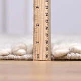 Close-up of the pile height of the cream Alora Area Rug, showing the hand-woven texture with a ruler. Pile