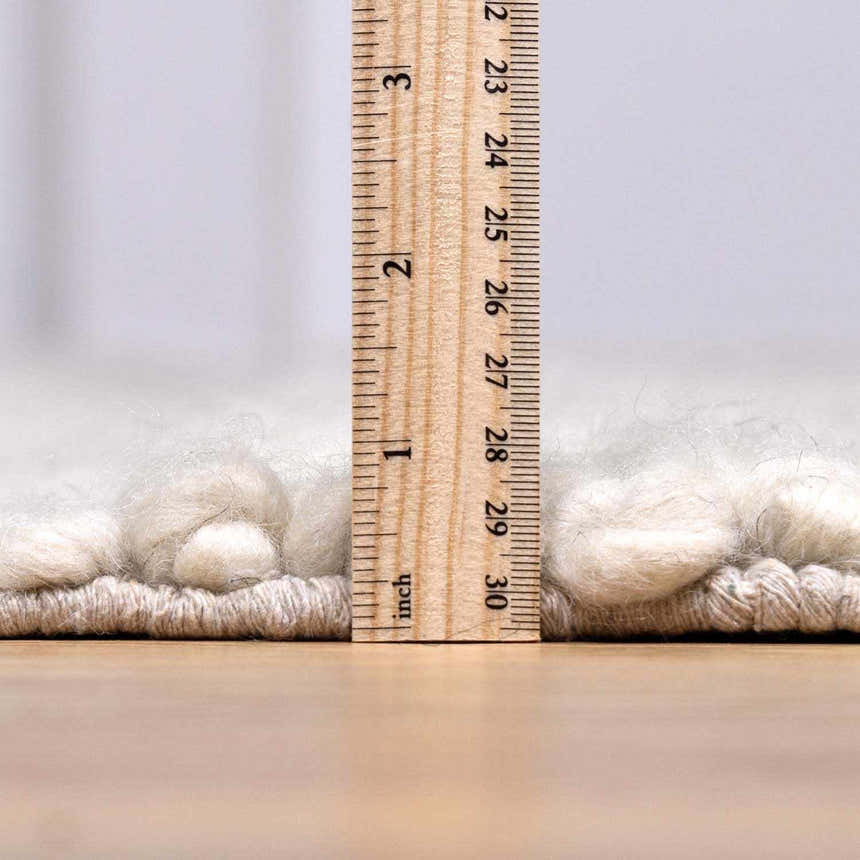 Close-up of the pile height of the cream Alora Area Rug, showing the hand-woven texture with a ruler. Pile